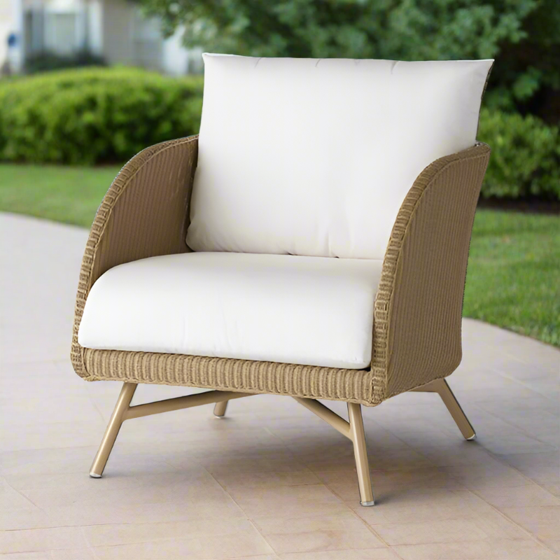 Beige wicker armchair with white cushions on a patio