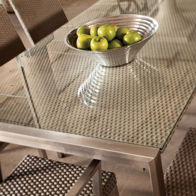 Dining table with glass top and metal frame, featuring a bowl of apples.
