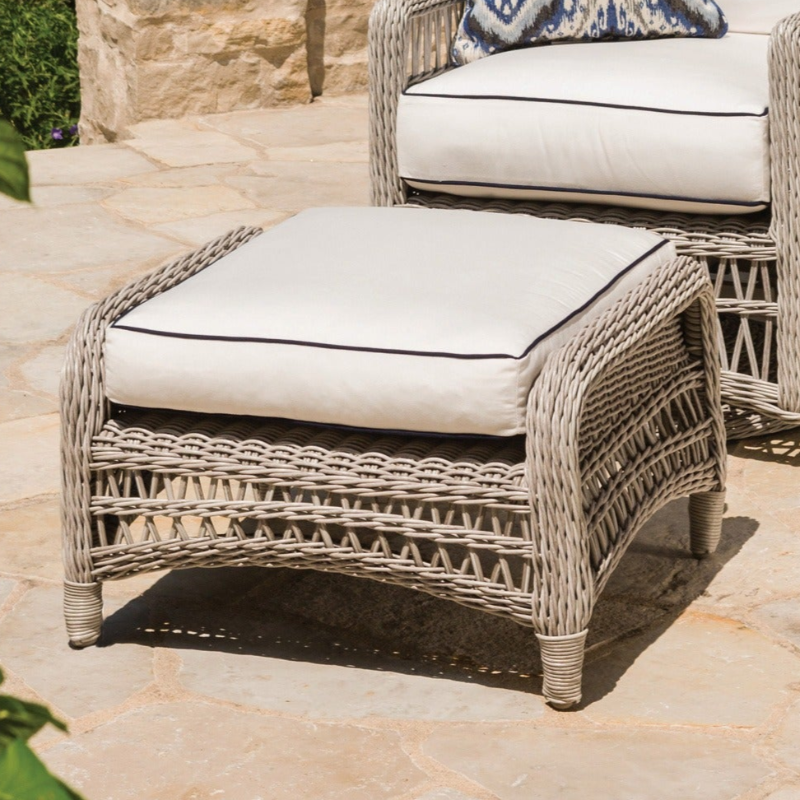 Wicker ottoman with white cushion on a stone patio