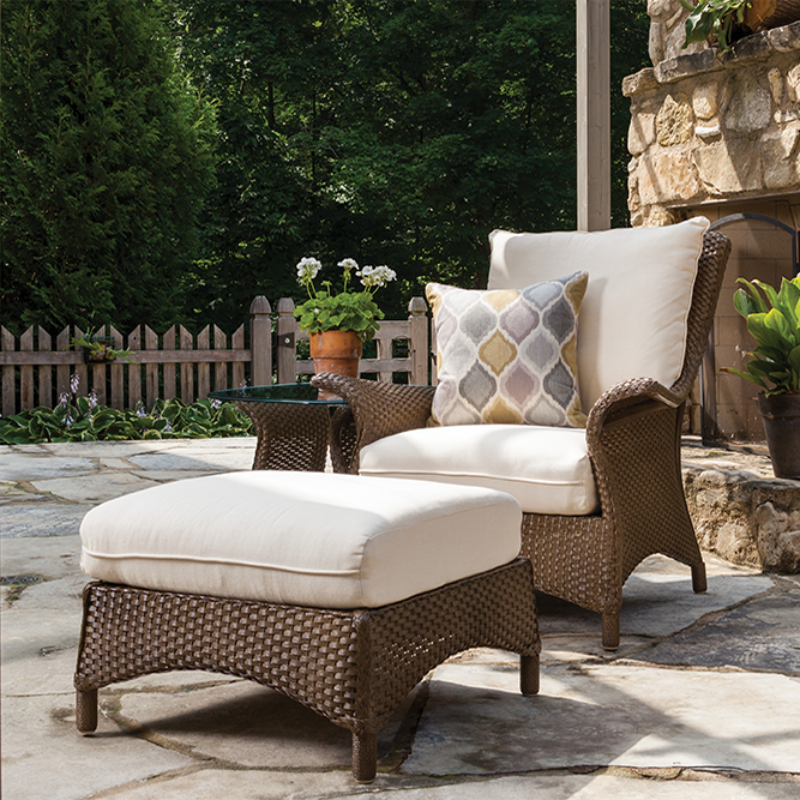 Outdoor patio set with wicker chairs and ottoman on a stone patio.
