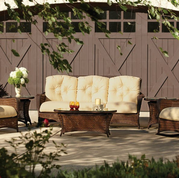Outdoor patio set with wicker furniture and cushions in front of a wooden fence.