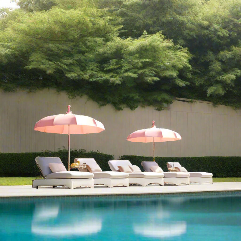 Poolside setup with lounge chairs and pink umbrellas by a pool.