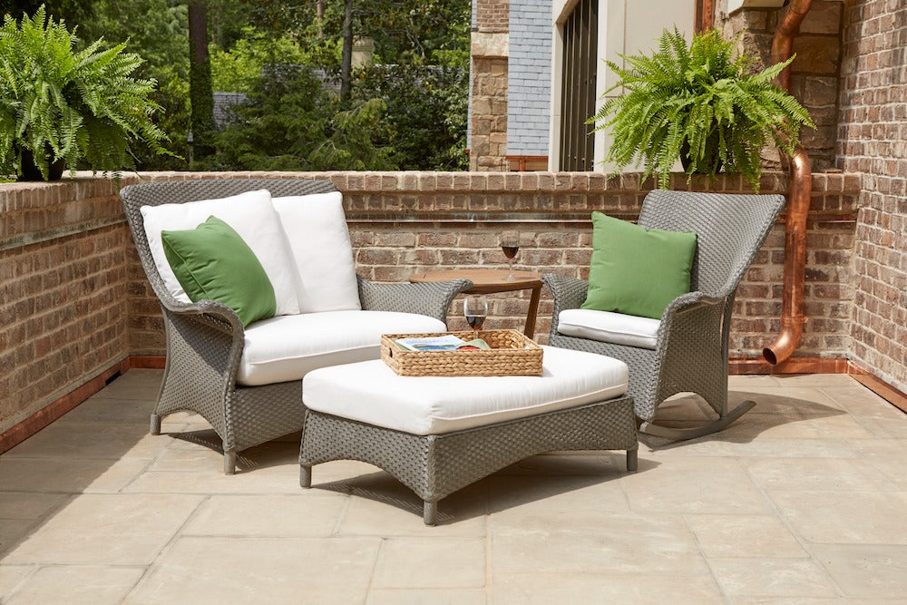 Outdoor patio set with wicker chairs, ottoman, and cushions on a tiled patio.