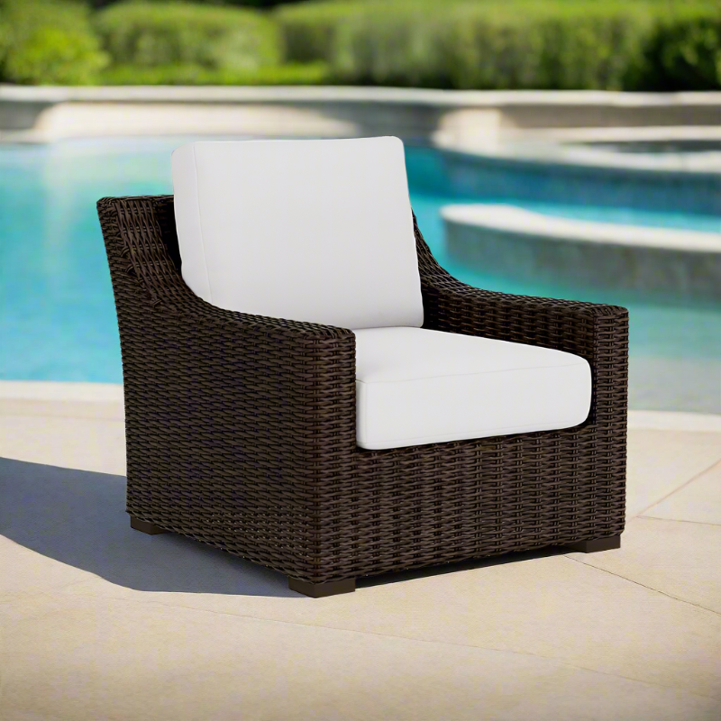 Brown wicker chair with white cushion by a pool