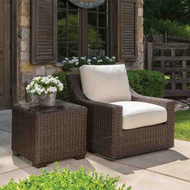 Outdoor patio set with wicker chair and table in front of a stone building.