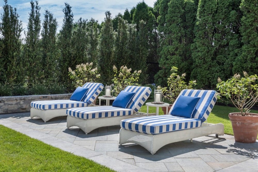 Three white lounge chairs with blue striped cushions on a patio surrounded by greenery.