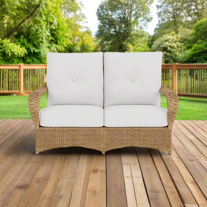 Wicker outdoor loveseat with white cushions on a wooden deck