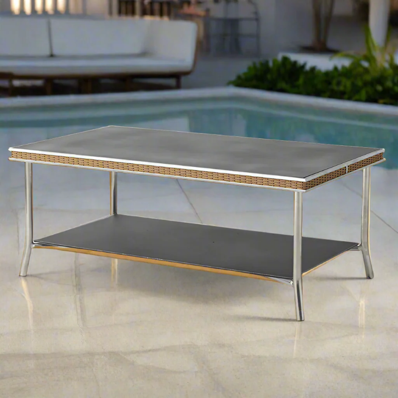 Outdoor coffee table with a reflective surface and wicker trim in a poolside setting.