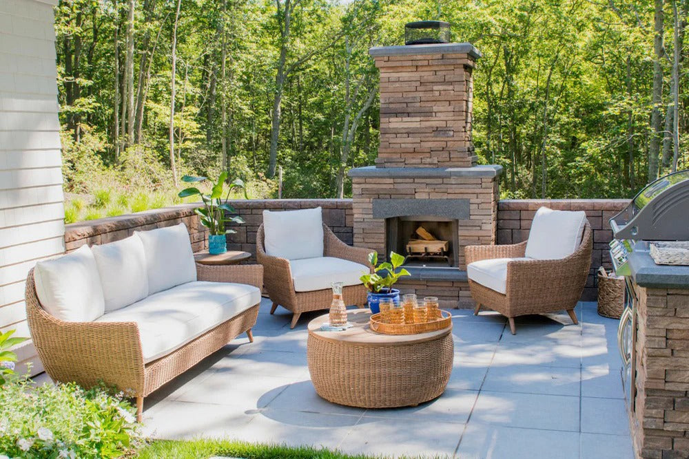 Outdoor patio with wicker furniture, fireplace, and grill in a wooded area