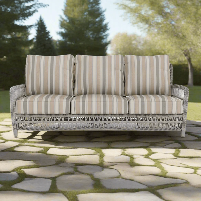 Outdoor sofa with striped cushions on a stone patio with trees in the background