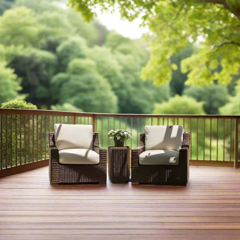 Two wicker chairs with white cushions on a wooden deck with a green forest background