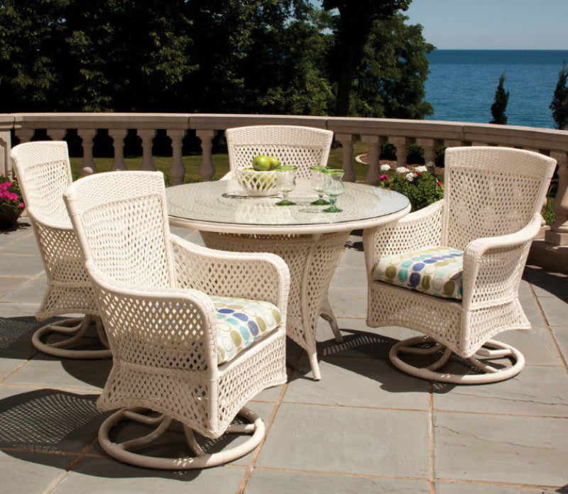 White wicker outdoor furniture set with cushions on a patio by the sea.