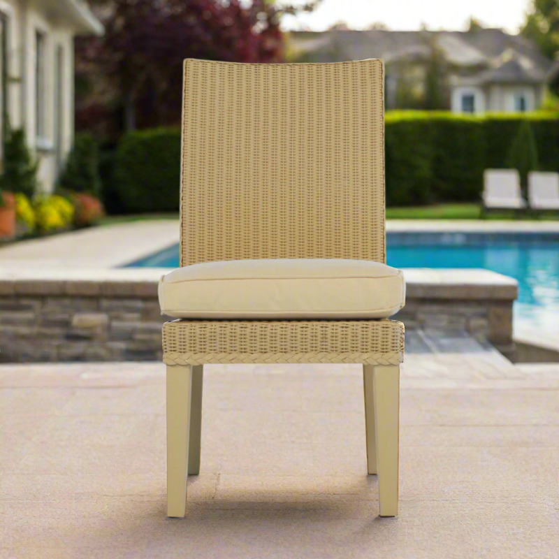 Beige wicker chair with cushion on a patio near a pool