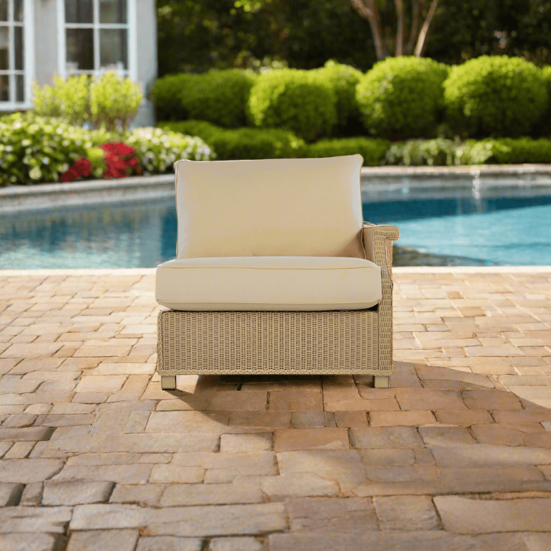 A beige Lloyd Flanders wicker left arm sectional chair with an overstuffed cushion, placed on a brick patio near a swimming pool.