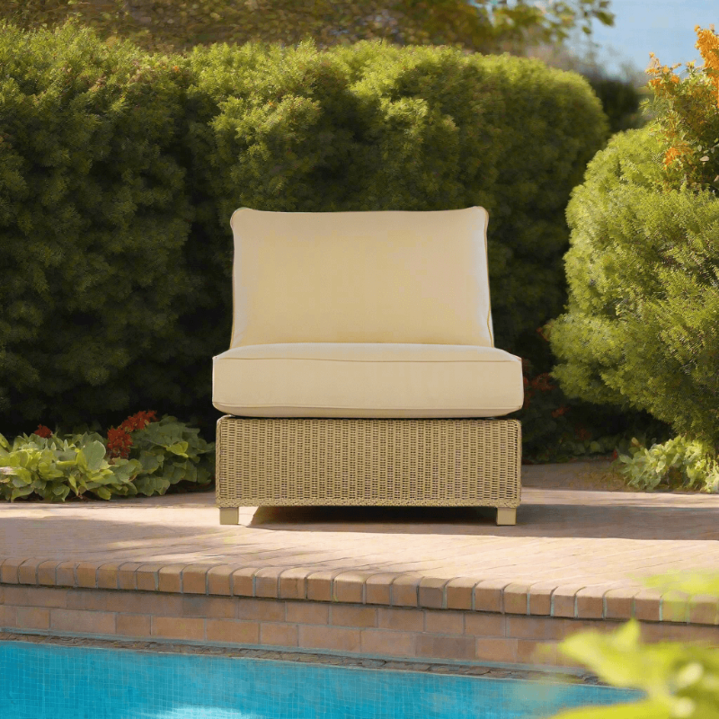 An armless sectional wicker chair with beige cushions placed beside a swimming pool.