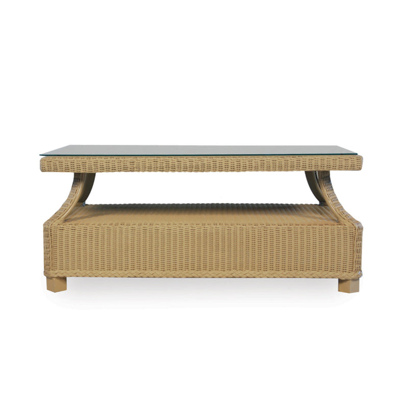 A rectangular wicker cocktail table with a flat, rectangular top and a curved, lower shelf. The table features a light brown wicker weave with a visible textured pattern.