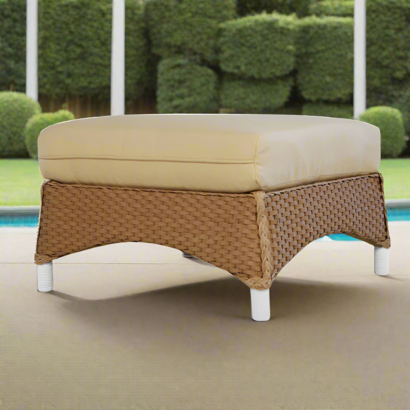 Wicker ottoman with beige cushion by a poolside