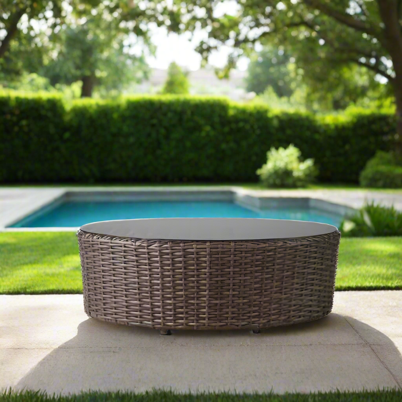 Wicker fire pit table on a patio with a pool and greenery in the background