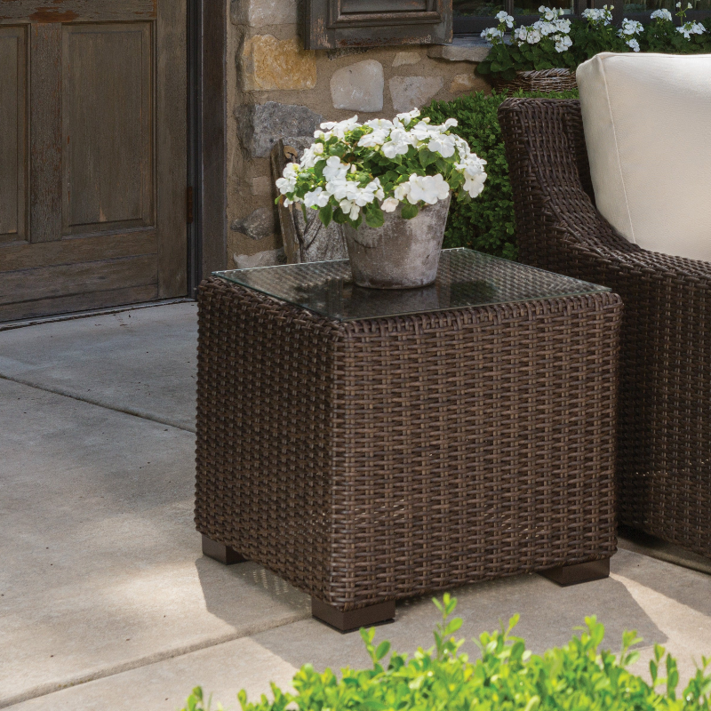 Wicker side table with a pot of white flowers on a patio