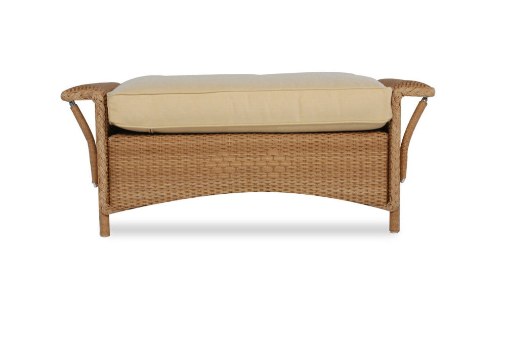A large wicker ottoman with a beige cushion on top and a brown wicker frame, designed for outdoor patio seating.