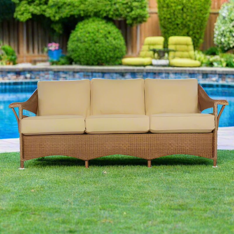 Beige cushioned outdoor sofa with wicker frame on grass by a pool