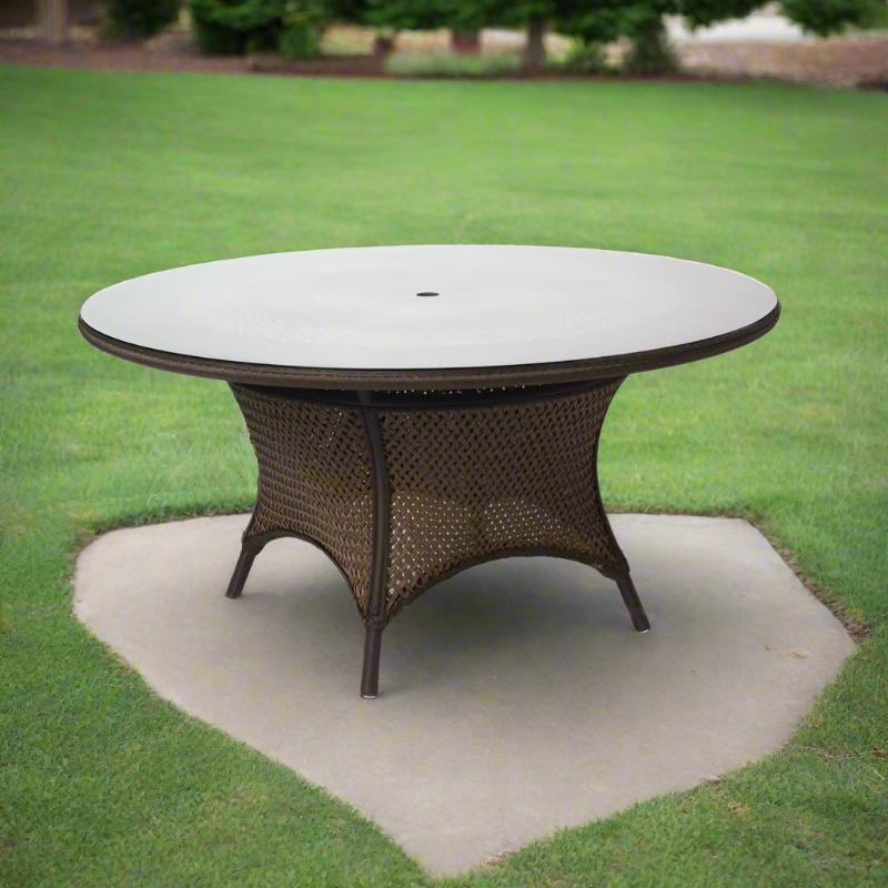 Round outdoor dining table with wicker frame on a concrete pad in a grassy area