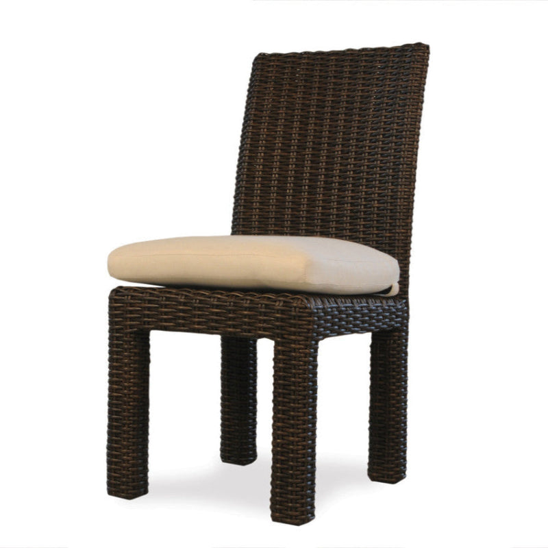 An armless dining chair with a brown wicker seat and backrest, and a white cushion on the seat.