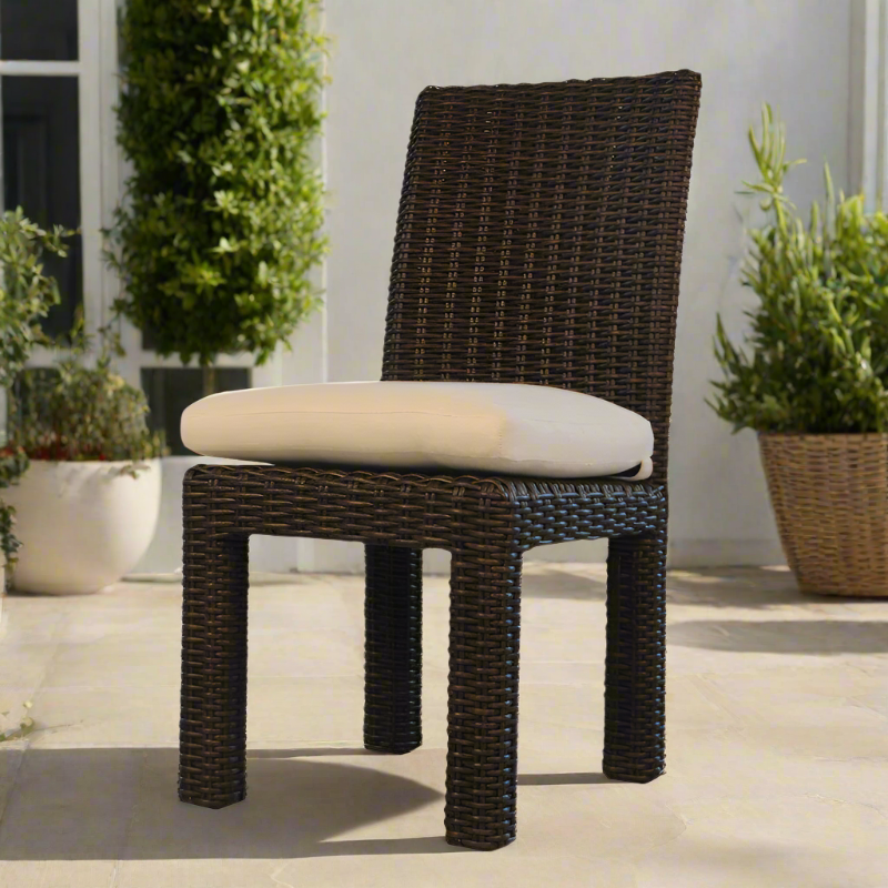 Wicker chair with a beige cushion on a patio with plants in the background