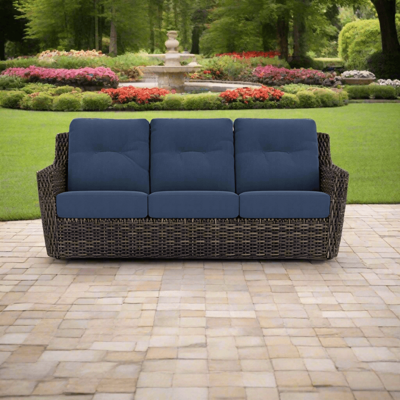 Wicker outdoor sofa with blue cushions on a patio in a garden setting
