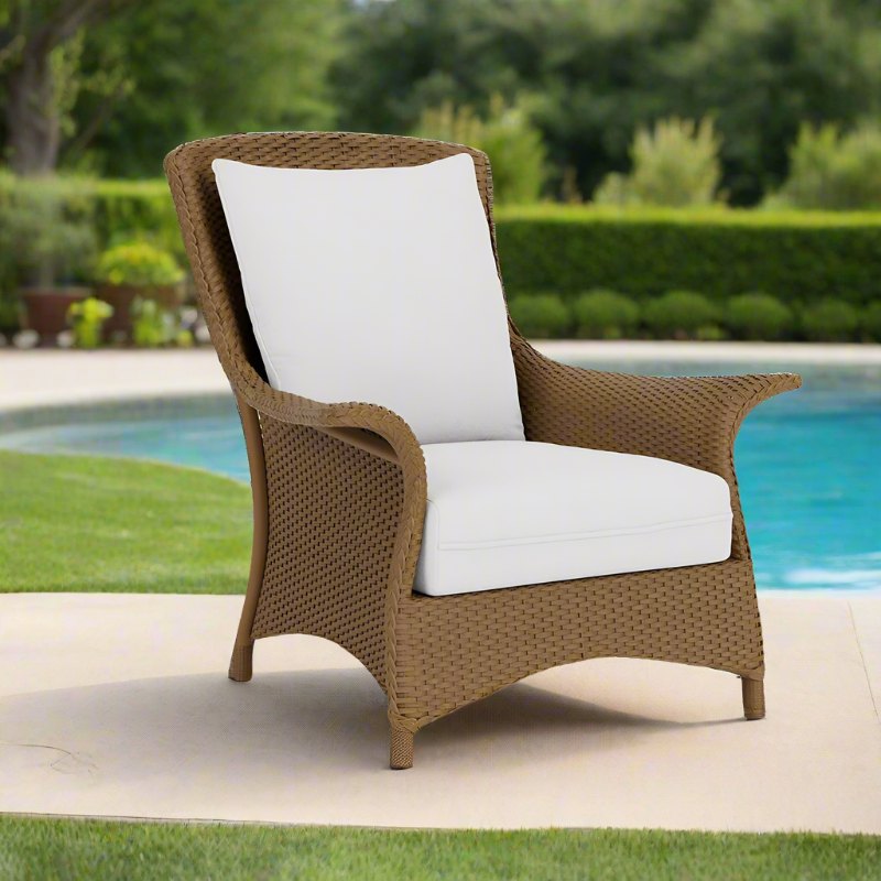 Brown wicker chair with white cushions by a poolside