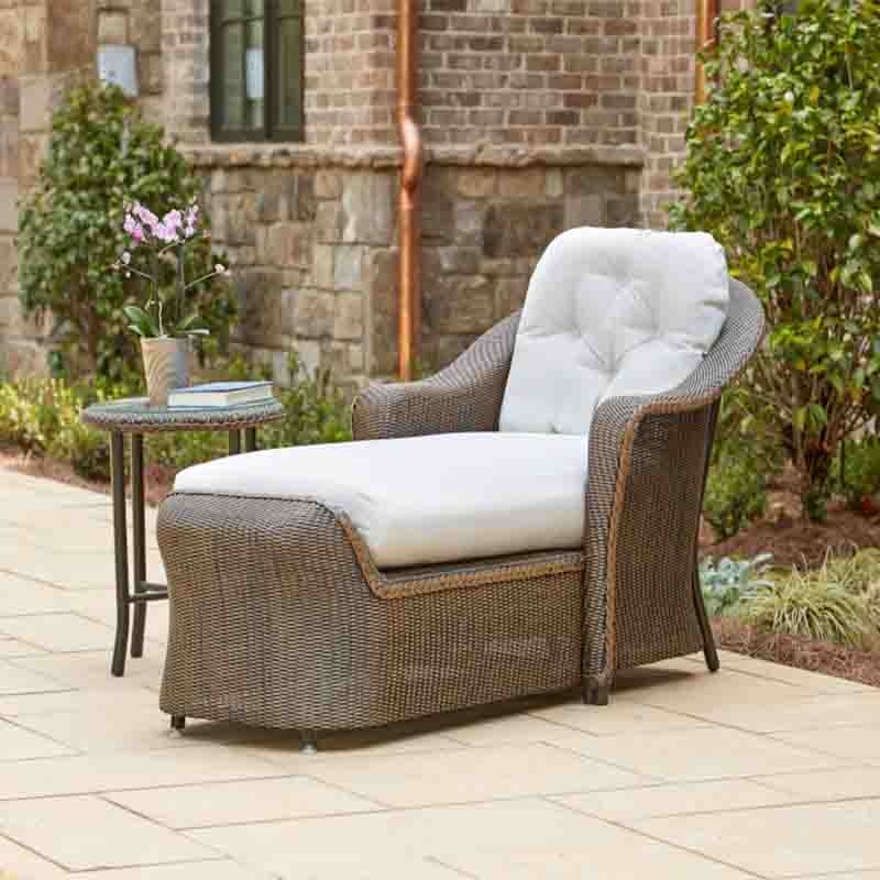 Wicker outdoor lounge chair with white cushions on a patio