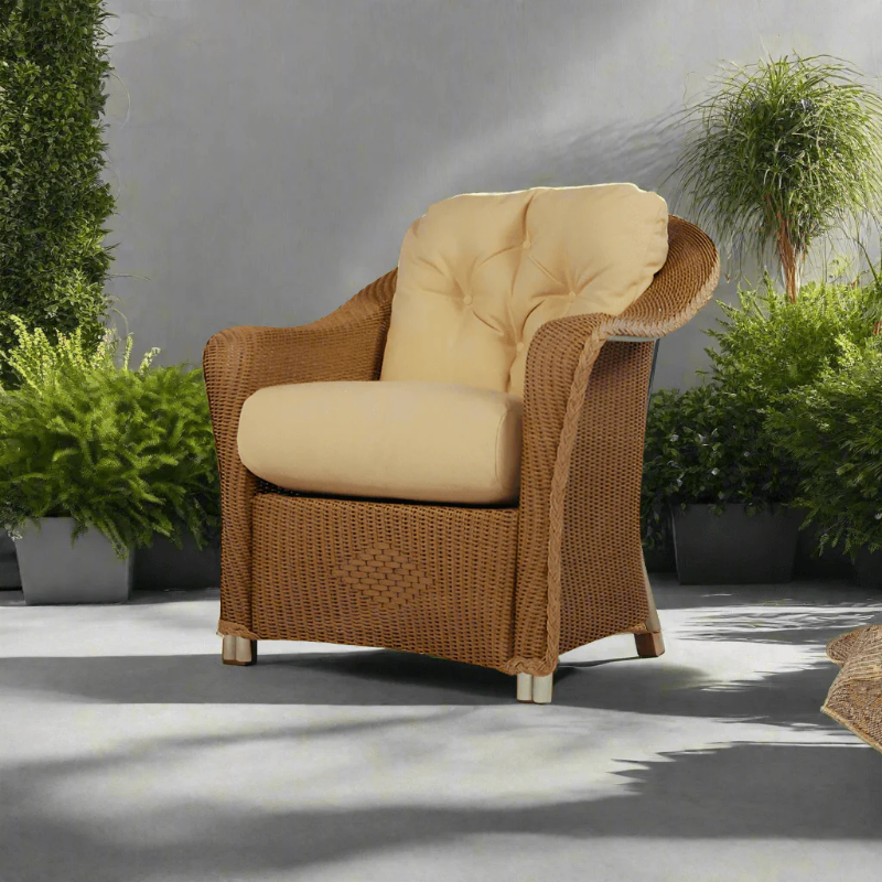 Wicker armchair with beige cushions in an outdoor setting with plants.
