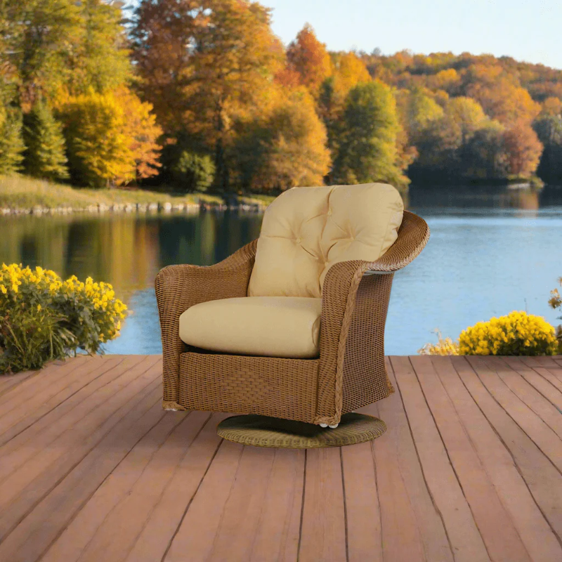 Wicker chair with beige cushions on a wooden deck by a lake with autumn trees.