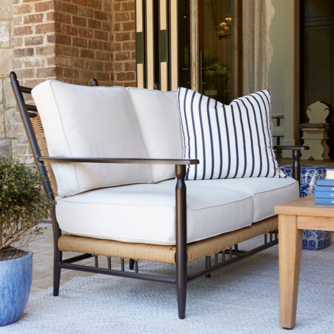 Outdoor patio setting with a white cushioned sofa, striped pillow, and wooden coffee table.