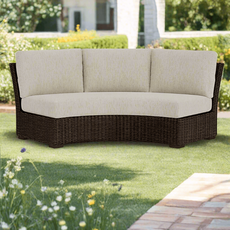 Wicker outdoor sofa with beige cushions on a grassy area