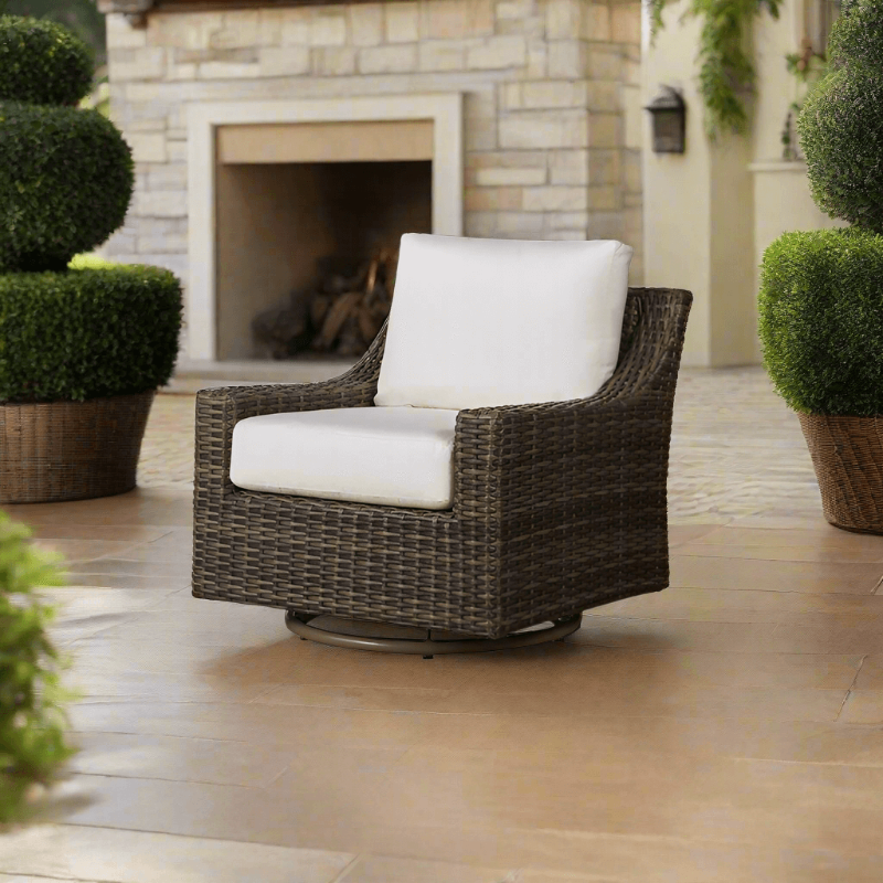 Wicker chair with white cushion on a patio with a fireplace and potted plants in the background