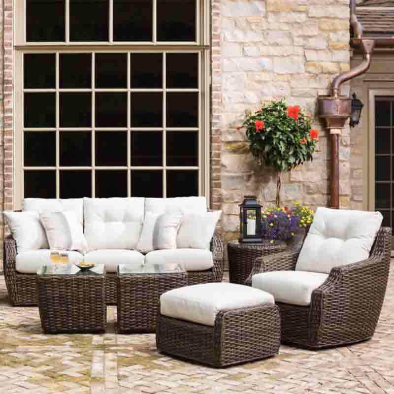Outdoor patio furniture set with white cushions in front of a stone wall.