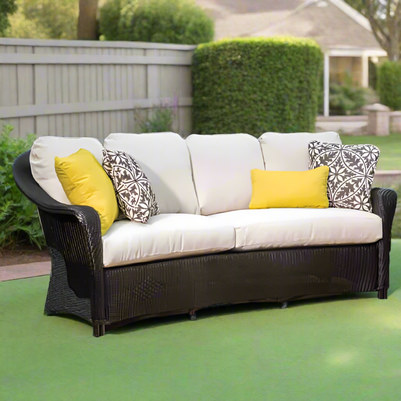 Outdoor sofa with white cushions and yellow and patterned throw pillows on a green patio.