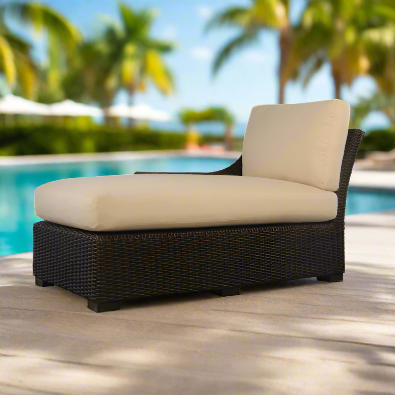 Outdoor lounge chair with beige cushion on a wooden deck by a pool with palm trees in the background.
