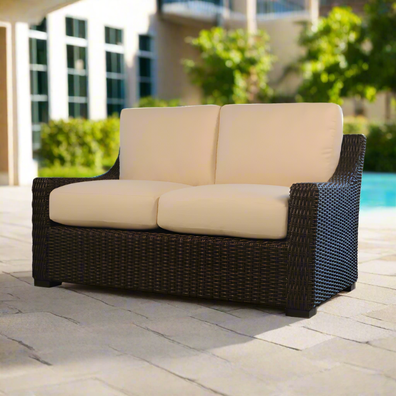 Wicker outdoor sofa with beige cushions on a patio near a pool.