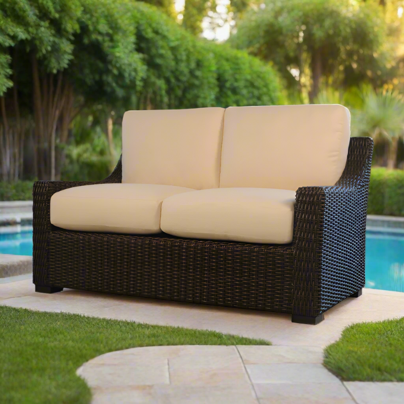 Beige cushioned outdoor sofa with wicker frame by a poolside