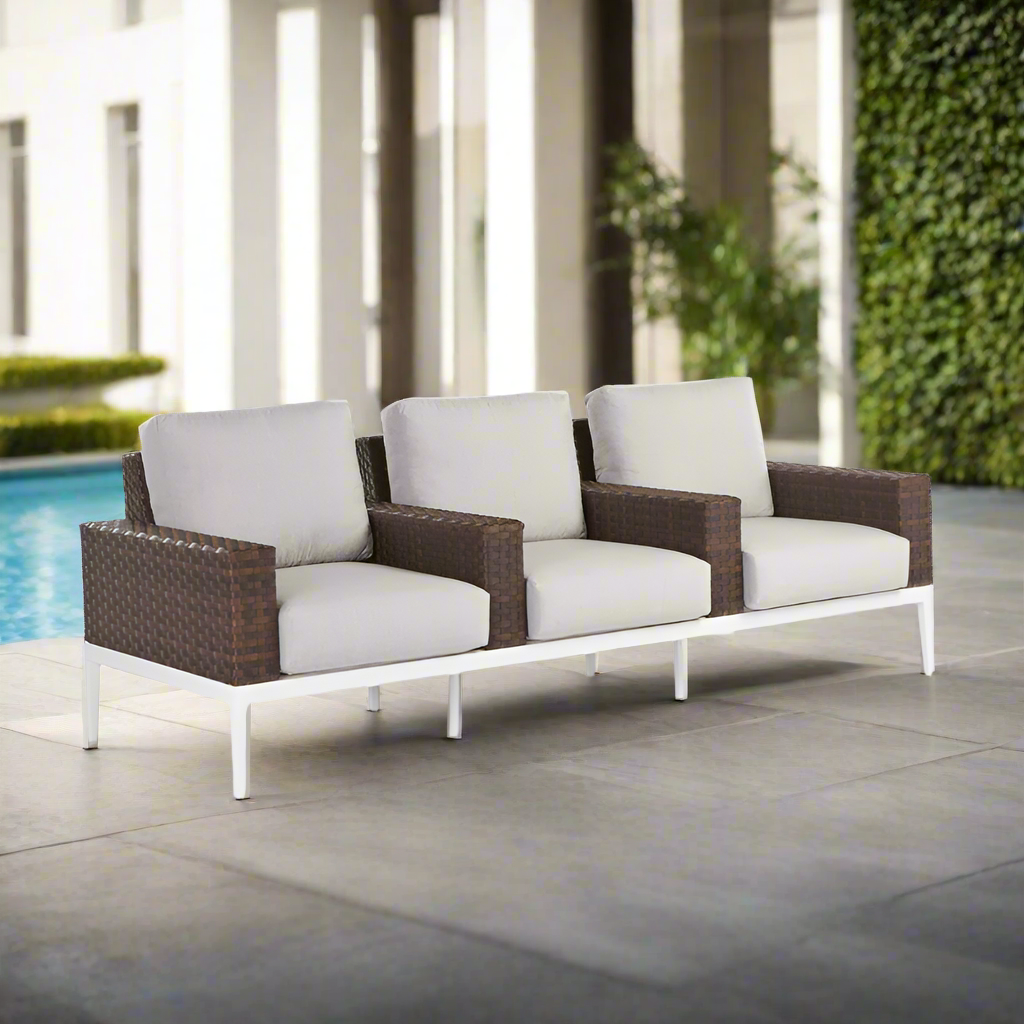 Outdoor sofa with wicker frame and white cushions by a poolside.
