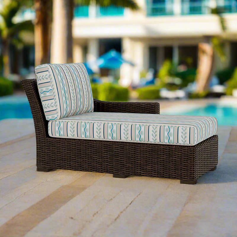 Outdoor wicker lounge chair with patterned cushions by a poolside.