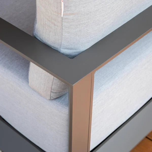 Close-up of a modern outdoor lounge chair corner with light gray textured fabric cushions and a dark gray metal frame with a rose gold accent leg.