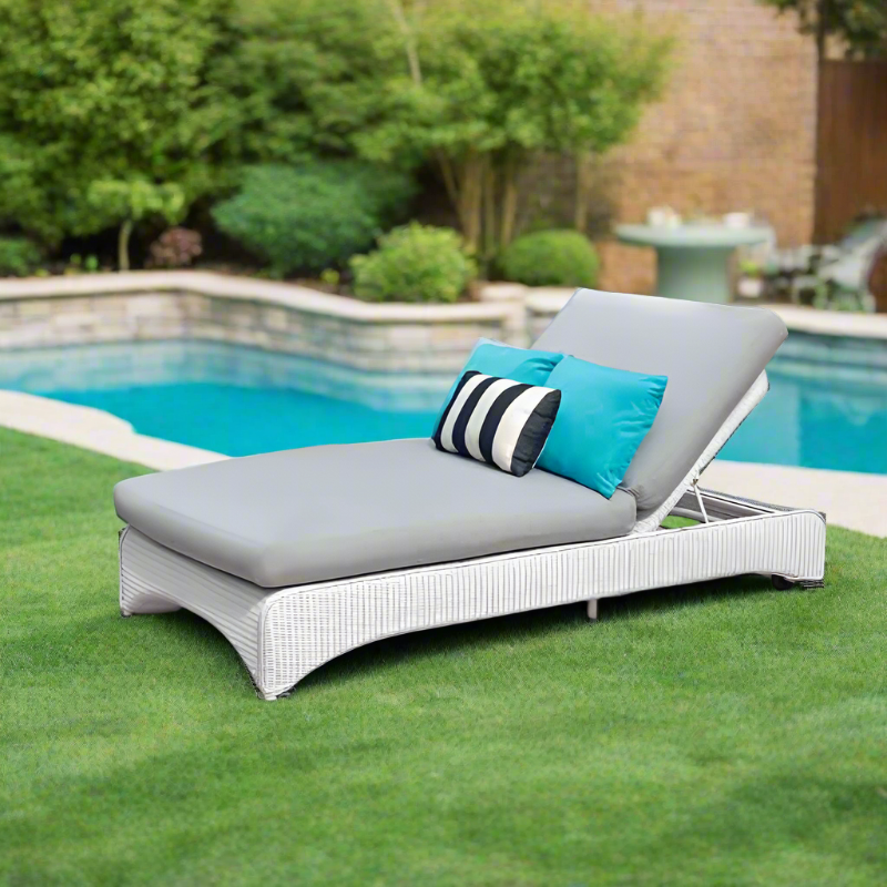 White outdoor lounge chair with gray cushions and blue and black striped pillows by a pool.