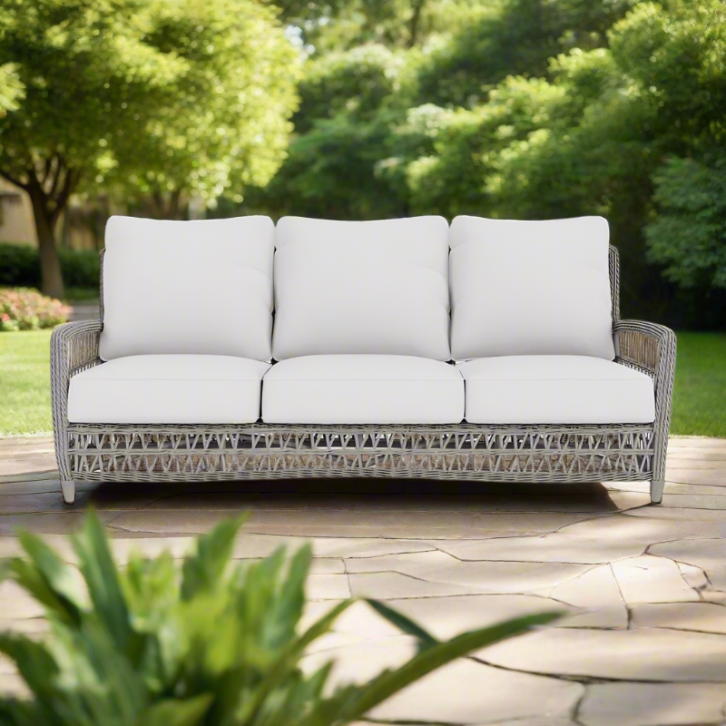 Outdoor sofa with white cushions on a patio with greenery in the background