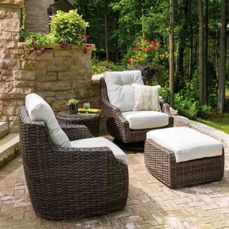 Outdoor patio set with wicker chairs and ottoman on a stone patio.