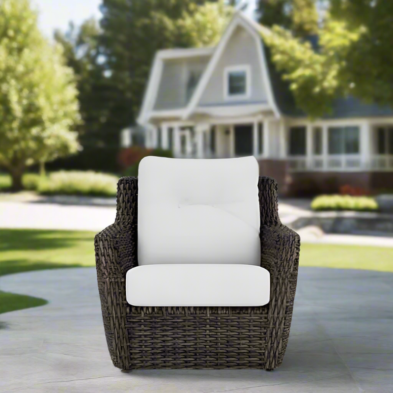 Wicker chair with white cushions on a patio in front of a house