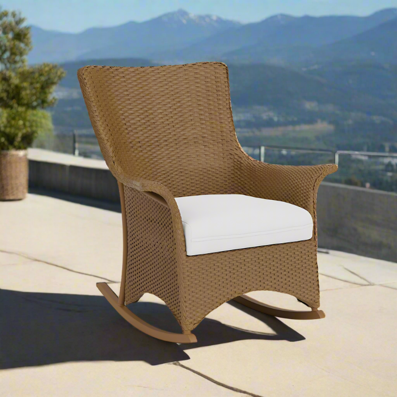 Brown wicker rocking chair with a white cushion on a patio with mountain views.