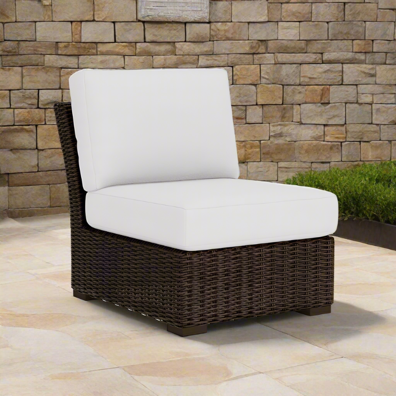 Wicker outdoor chair with white cushions against a stone wall.